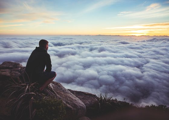 Man on cliff looking at clouds observing meditation