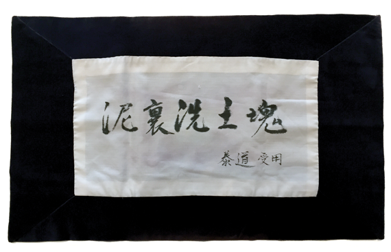 The author's rakusu cover with calligraphy by Maezumi Roshi that reads "To wash a clod of earth in the mud."