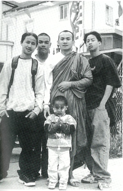 Ajahn Keerati Chatkaew poses before an American flag with Johnny Kammanh (left), Dom Phommachak, Khambei Vobouxasinh (right), and three-year old Andrew Khammanh. Ajahn Keerati is beloved among the youth of Wat Chansisamakidham for his relentless humor and his ability to imitate street slang. Copyright Bob Easton-Waller.