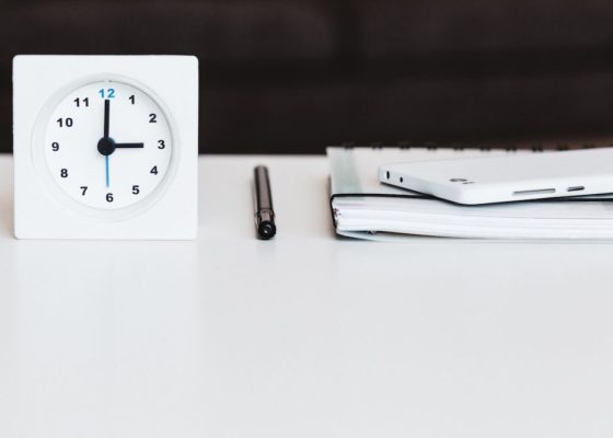 clock, pen, phone and notebook on a white table