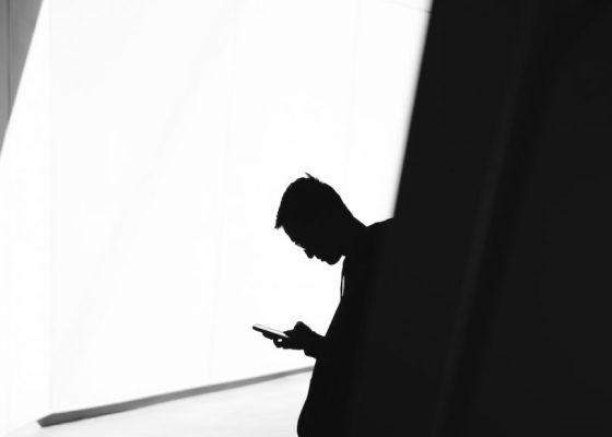 Silhouette of a person looking down at their cell phone