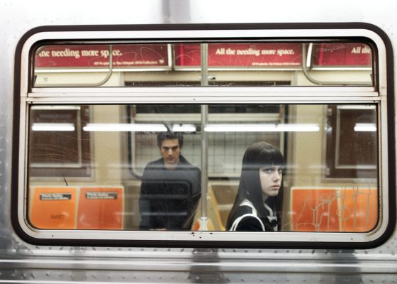 A girl sits on a train, stared at by man