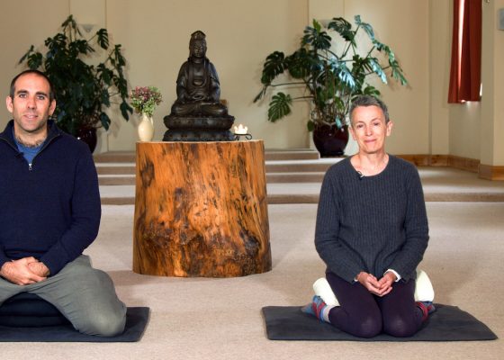 Beyond the Inner Critic course teachers Laura Bridgman and Gavin Milne seated in a meditation hall with a Buddha statue